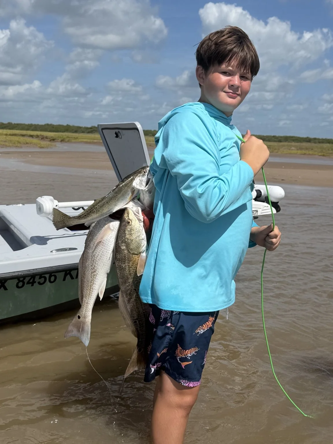 Young angler holding a stringer of fish beside a boat near Sargent, Texas