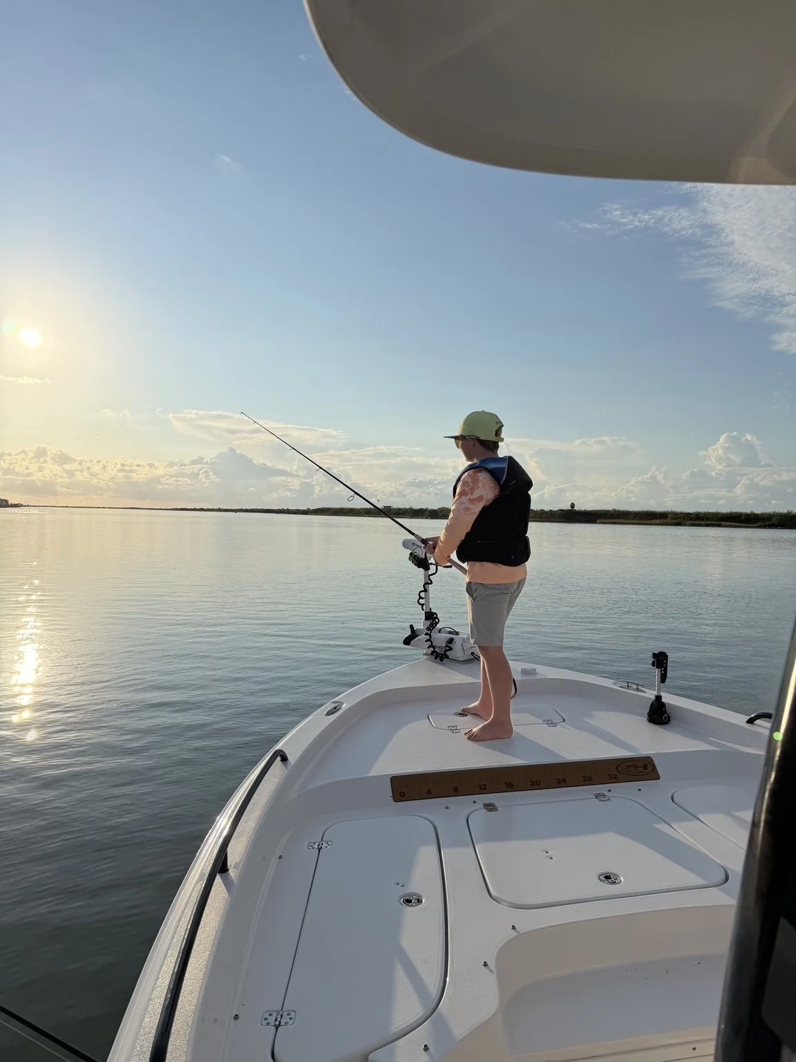 Young angler fishing from the bow of a boat at sunset